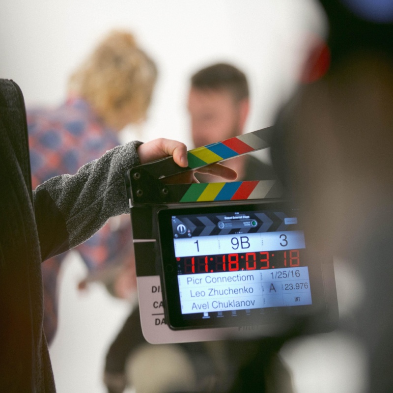 A digital clapper board with 2 people in the background